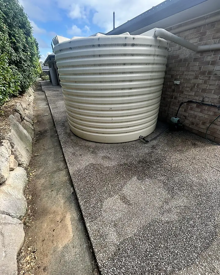 An exposed aggregate path beside a rainwater tank, stained grey