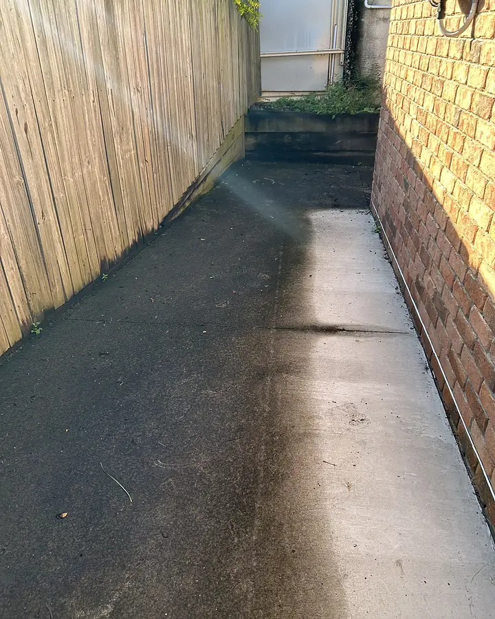 A narrow concrete side path dark with grime and growth before pressure cleaning