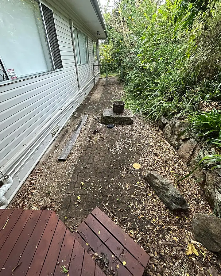 A side path beside a weatherboard house covered in leaf litter and grime