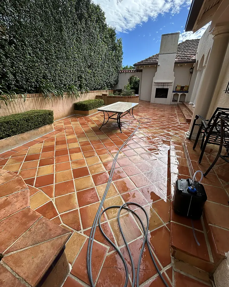 A large terracotta-tiled patio with a fireplace, freshly pressure cleaned