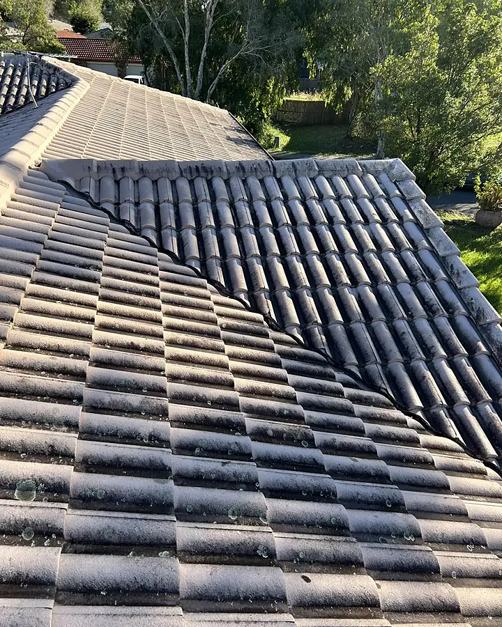 A concrete tile roof half cleaned, the clean side and the dark side split along a diagonal