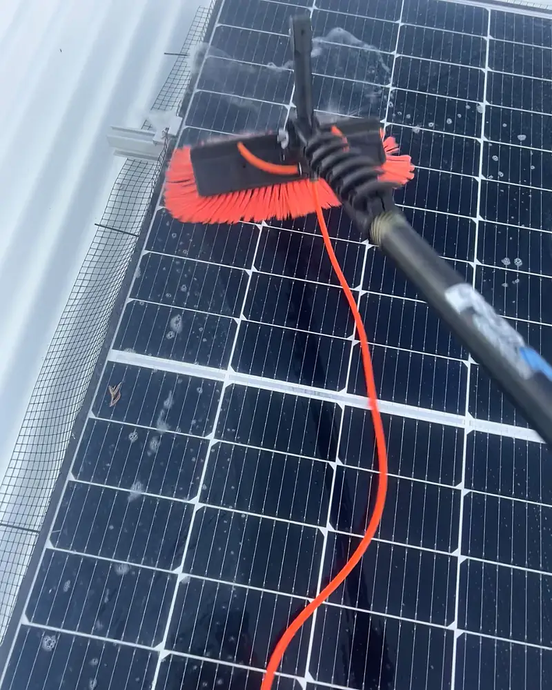 A soft brush on a long pole cleaning a solar panel with deionised water
