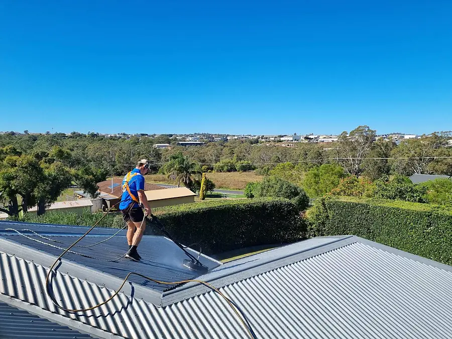 A Posh Wash crew member in harness cleaning a metal roof high above a Brisbane suburb