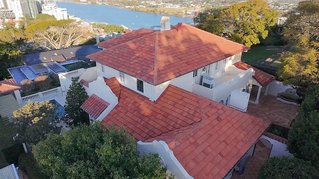 A cleaned red tile roof on a large white house with the Brisbane River behind