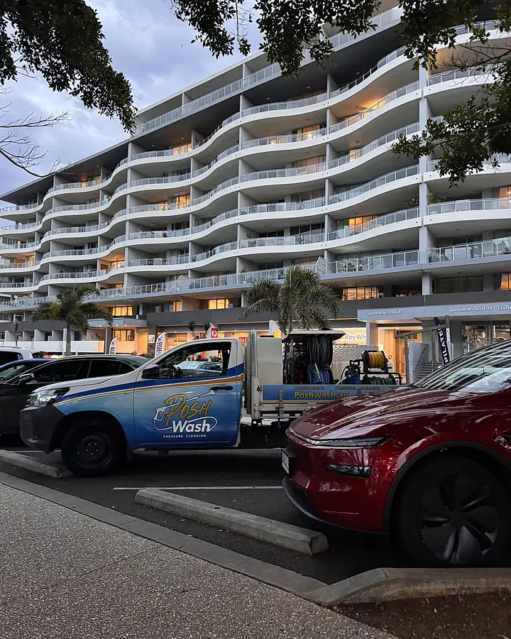 The branded Posh Wash ute parked outside a curved white apartment building at dusk