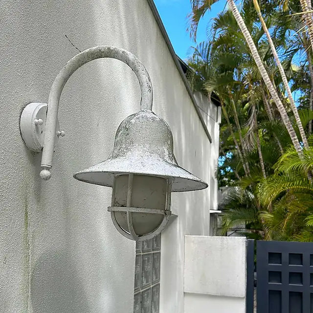 A wall-mounted lamp and white wall grimy with mould before washing
