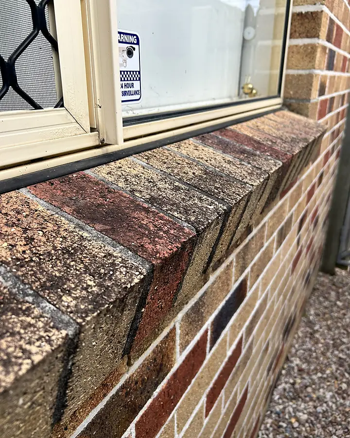 A brick window ledge and frame thick with grime before cleaning